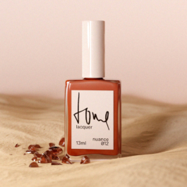 Nagellack-Flacon auf Sandboden mit Edelsteinen